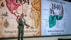 Dr. Miguel Stanley on stage beside a historical map dividing medicine and dentistry